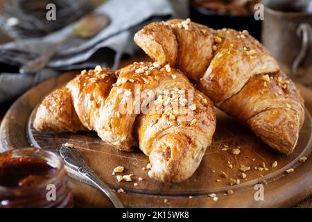 Delicious vegan croissants with crushed hazelnuts for breakfast on dark rustic wooden cutting board Stock Photo