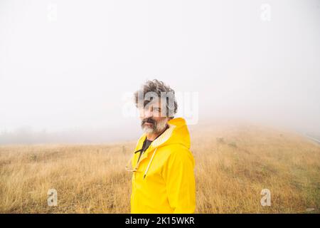Side view middle aged bearded man in yellow raincoat walking while spending misty morning in dry Irati Valley in Navarre, Spain Stock Photo