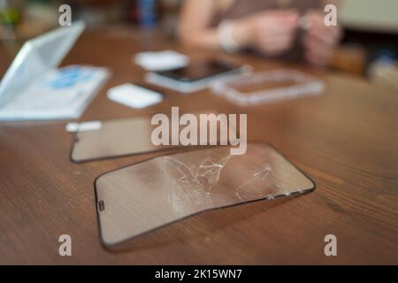 Soft focus of cracked protective glass for smartphone screen placed on desk in repair workshop Stock Photo