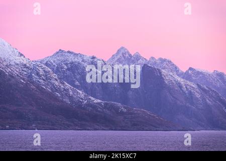 Scenic aerial landscape of rocky mountains with sharp peaks covered with snow near calm sea against sunset sky in Norway Stock Photo