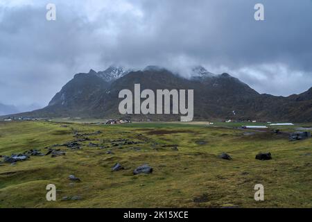 Grassy terrain leading to village with small cottages located in mountainous valley in Lofoten Islands in Norway against overcast sky Stock Photo
