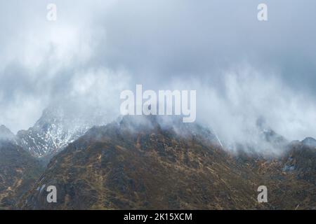 Range of rough rocky mountains with uneven surface covered with snow located against overcast cloudy sky in nature on winter day in Lofoten, Norway Stock Photo