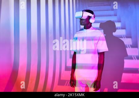Young black man in white t shirt with modern VR headset in studio with bright colorful neon illumination Stock Photo
