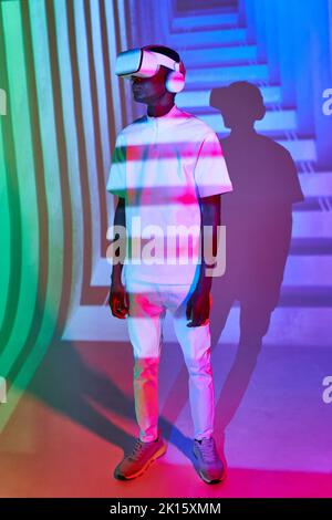 Young black man in white t shirt with modern VR headset in studio with bright colorful neon illumination Stock Photo