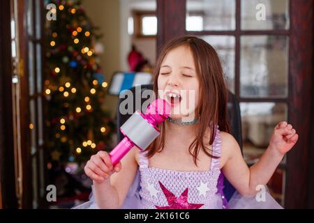 a little girl in costume sings loudly into a microphone at home Stock Photo