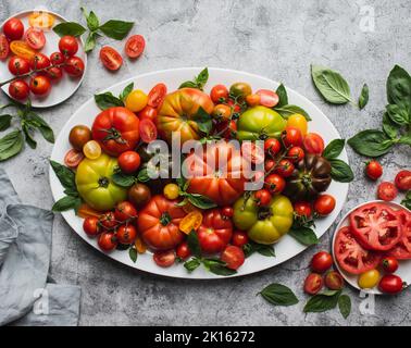 Top view of platter of tomatoes and basil on grey background.. Stock Photo