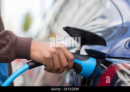 a hand holding charging cable at an e charging station Stock Photo