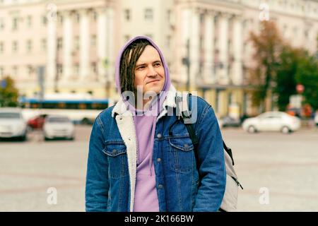 Young handsome man with dreadlocks in casual clothes posing on busy street in downtown Stock Photo