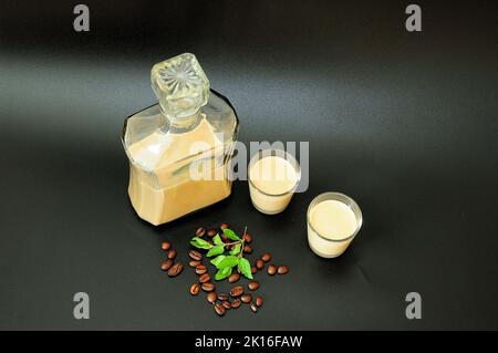Creamy coffee liqueur, homemade alcohol in a bottle and two glasses on a black background, next to mint leaves and coffee beans. Close-up. Stock Photo