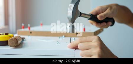 man using hammer hammering a nail into wooden boards, assembling or repairing furniture at home. DIY, Renovation, repairing and development home or ap Stock Photo