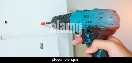 man using a cordless screwdriver assembling furniture at home, Carpenter working with electric screwdriver on the work Stock Photo
