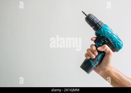 man hand holding cordless screwdriver with wall background, Carpenter working with electric screwdriver on the work Stock Photo