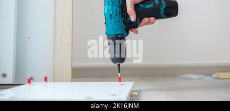 man using a cordless screwdriver assembling furniture at home, Carpenter working with electric screwdriver on the work Stock Photo
