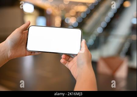 Close-up image, A female uses her smartphone to take a picture inside of the shopping mall. A woman holding a white screen mobile phone over blurred s Stock Photo