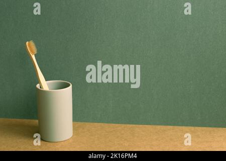 Bamboo toothbrush in a cup on brown shelf. green wall background. bathroom interior Stock Photo