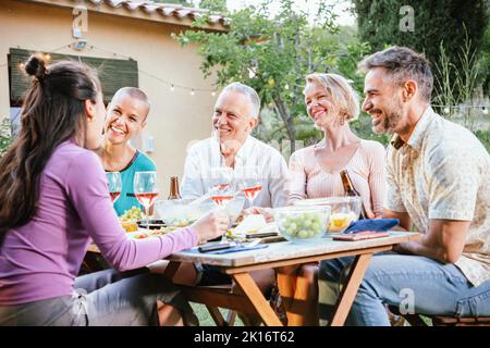 Group of mature adult friends toasting his wine glasses and beers and having fun in a dinner party at the back yard. Lifestyle concept. Stock Photo