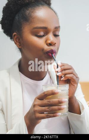 Portrait of a dreamy woman drinking ice coffee sitting in cozy cafeteria, enjoying leisure time. Freelancer female enjoying break with latte coffee Stock Photo