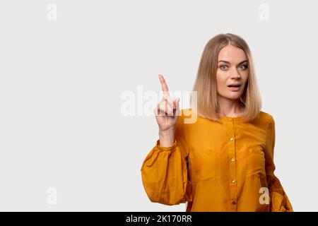 Warning gesture. Disturbed woman. Shock discovery. Aha moment. Portrait of worried confused lady in yellow blouse pointing up isolated on light neutra Stock Photo