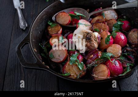 Pan roasted vegetable dish with caramelized red radish, red onions, garlic, olive oil and parley. Served and cooked in a cast iron pan Stock Photo