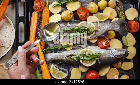 Preparing sea bass fish for cooking on the grill with aromatic herbs and vegetables on wooden board top view Stock Photo