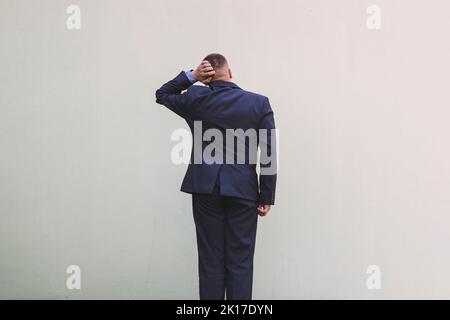 young handsome man feeling clueless and confused, thinking a solution, with hand on head, rear view. copy space for text. The concept of choice Stock Photo