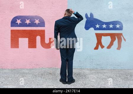 man thinks in the background wall with symbols of US parties. In American politics US parties are represented by either the democrat donkey or republi Stock Photo