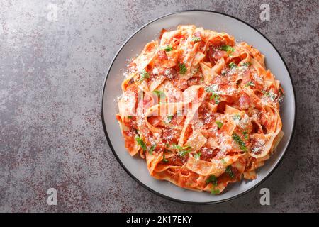 Pappardelle pasta with bacon and tomato sprinkled with parmesan cheese and chopped parsley closeup in the plate on the table. Horizontal top view from Stock Photo