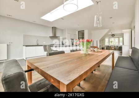 Table with chairs and flowers located near lounge area and kitchen in spacious room of contemporary apartment Stock Photo