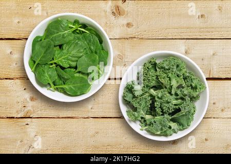 Two white bowls one containing spinach leaves and one containing chopped kale leaves. Shot from above on a rustic wooden background Stock Photo