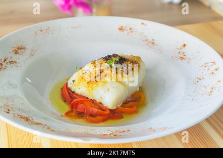 Delicious baked cod with roasted red pepper on wooden table. Stock Photo