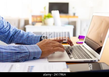 Hands of senior biracial businessman using laptop sitting at desk at home Stock Photo