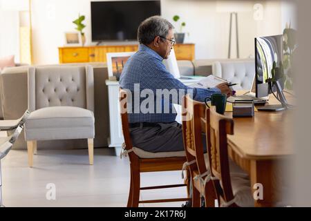 Senior biracial businessman using computer sitting at desk at home Stock Photo