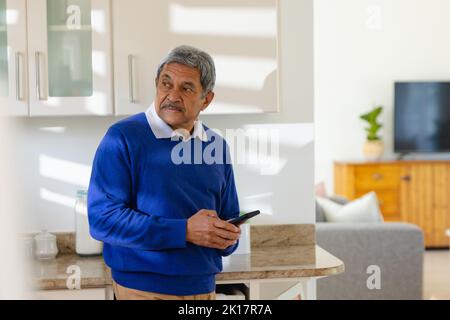 Senior biracial man using smartphone in kitchen at home Stock Photo