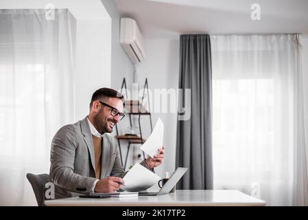 Smiling adult man with glasses, checking the company income, reading documents, sitting. Stock Photo
