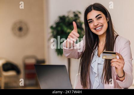 Optimistic young long haired businesswoman, giving approval, showing credit card. Stock Photo