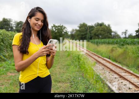 Content young ethnic lady listening to song and using smartphone in nature Stock Photo