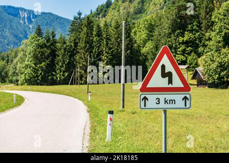 Triangular white and red road sign of winding roads ahead, mountain road with series of dangerous curves for three kilometers. Slovenia, Europe. Stock Photo