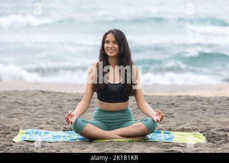 Content young ethnic woman sitting on seashore in Padmasana pose during yoga practice Stock Photo