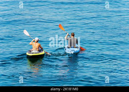 A man and a woman aboard their kayak, paddling in the blue Mediterranean sea, on a sunny summer day. Gulf of La Spezia, Liguria, Italy, Europe. Stock Photo