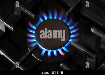 Gas burner with a blue flame on a black kitchen stove, with a cast-iron grate, top view, selective soft focus. gas crisis. Stock Photo