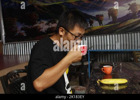 A guy is wearing a glass and drinking tea in morning time , putting a banana , eating fruit Stock Photo