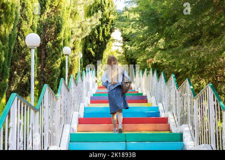 A woman climbs up colored, multi-colored stairs. Concrete colored steps Stock Photo