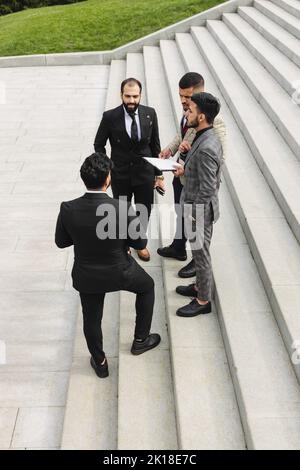 Business people outdoor meeting. A group of men in suits stands against the backdrop of the urban steps of a large staircase. Working break. Teamwork Stock Photo