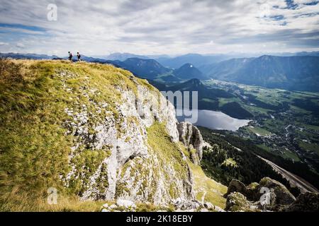 Two mountain climbers on a ridge on the way up to the summit of Loser mountain, with Altaussee, Austria, and the Altausseer See in the background Stock Photo