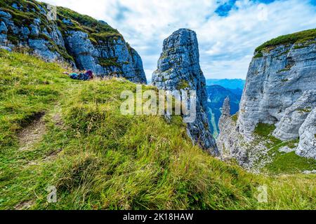 View of a female hiker resting on the precipice near the Loser peak, from which some prominent jags are rising, Ausseer Land, Styria, Austria Stock Photo