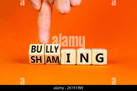 Shaming and bullying symbol. Concept words Shaming and Bullying on wooden cubes. Businessman hand. Beautiful orange table orange background. Business Stock Photo