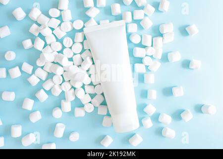 Mockup white squeeze bottle cosmetic tube and and white little marshmallows on blue background. Daily cream, gel, skin care, sunscreen, moisturizer. F Stock Photo