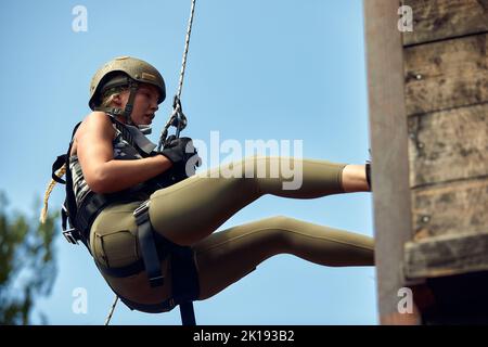 Soldier training rappel with rope. Military woman does hanging on climbing equipment Stock Photo