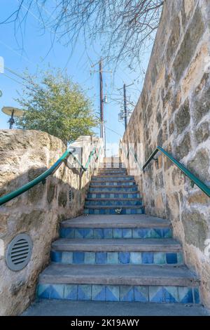San Antonio, Texas- Narrow stairs with blue ornate riser tiles and wall-mounted handrails. Staircase outdoors against the trees, electrical posts, and Stock Photo