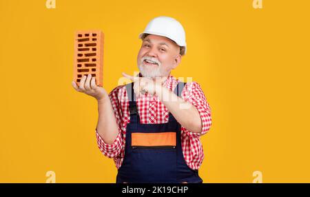 smiling senior man bricklayer in helmet on yellow background Stock Photo
